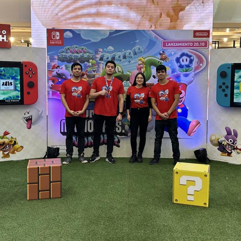Cuatro integrantes del equipo de terreno de Uptiva, con poleras rojas, en el stand de Super Mario Bros Wonder de Nintendo en un mall